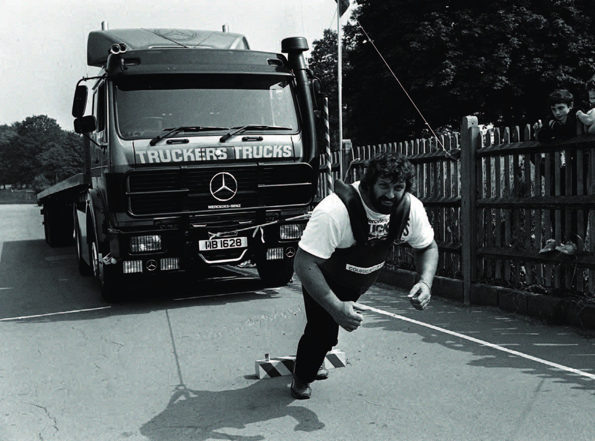 Black-and-white action photograph of strongman Geoff Capes pulling a lorry.