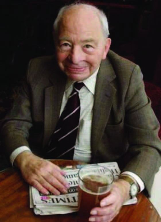 Colour portrait of Inspector Morse creator Colin Dexter seated with a newspaper and a pint.