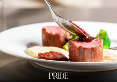 A chef in black gloves spoons sauce over a fillet of meat on a white plate