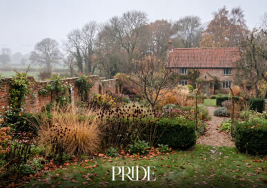 A walled cottage garden in autumn with ornamental grasses, seedheads and a red-brick house in the mist