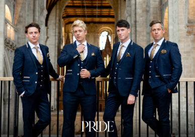 The four members of G4 in navy three-piece suits standing at a balustrade inside a cathedral